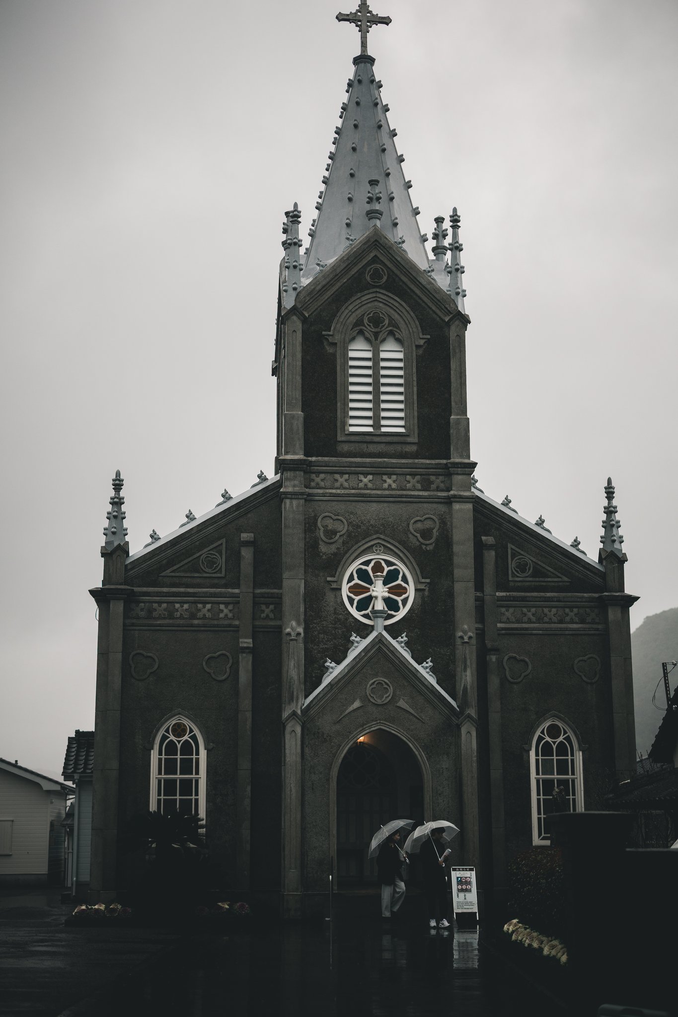 The front of Sakitsu Church in the rain, with two visitors under umbrellas at the entrance