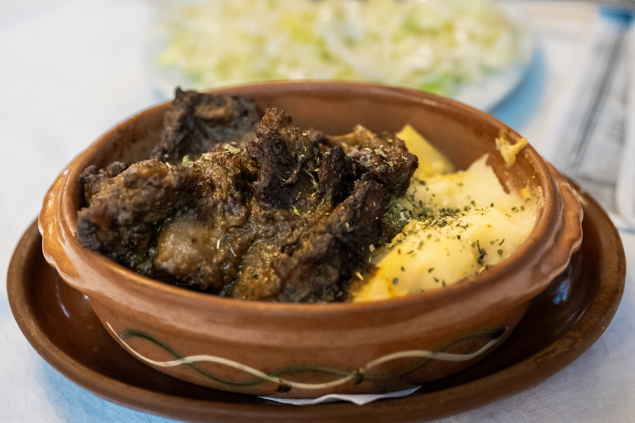 Large pieces of beef goulash in thick dark sauce beside mashed potatoes in a brown ceramic dish.