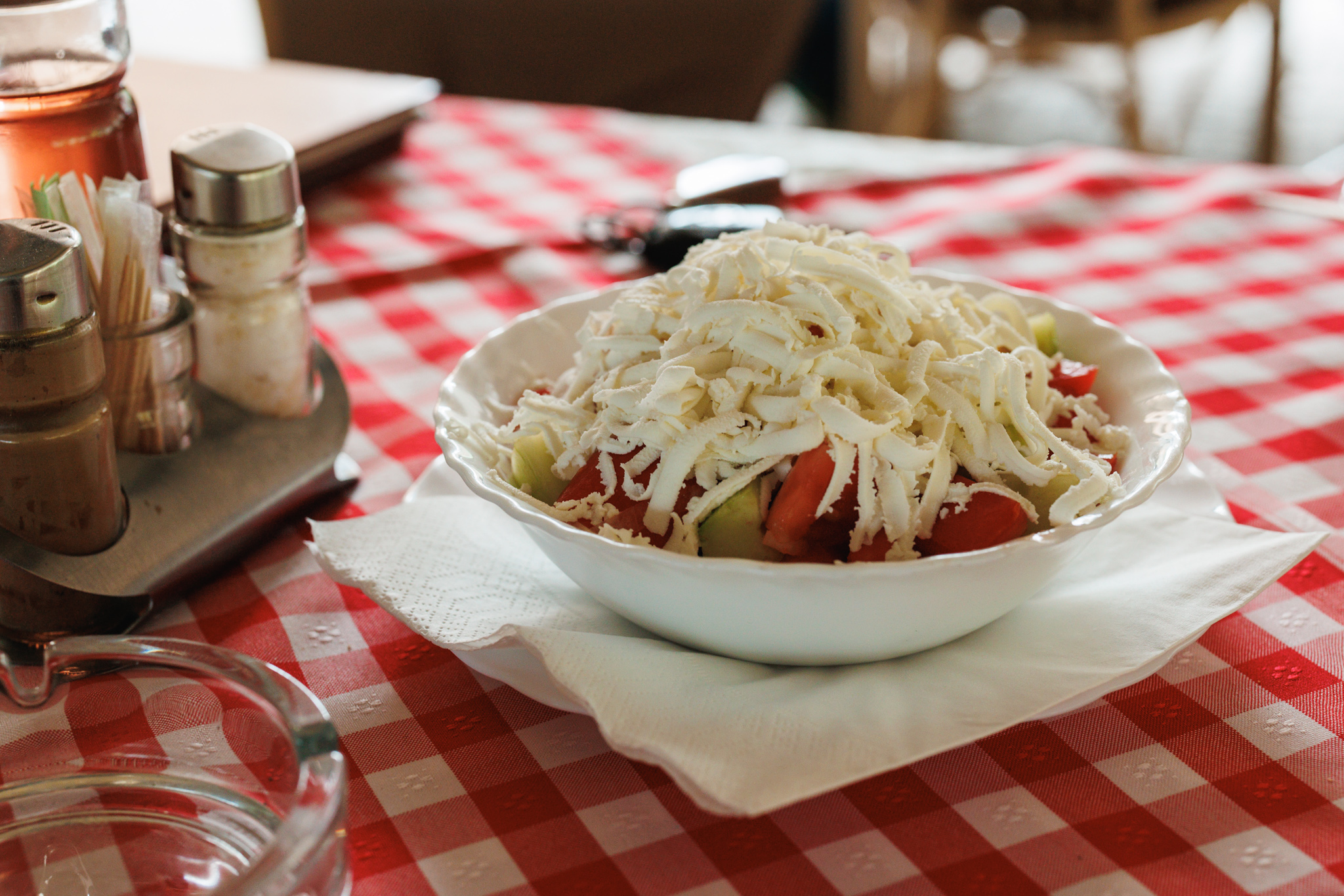Shopska salad with grated white cheese covering tomato and cucumber in a white bowl at Balkan Ekspres 021.