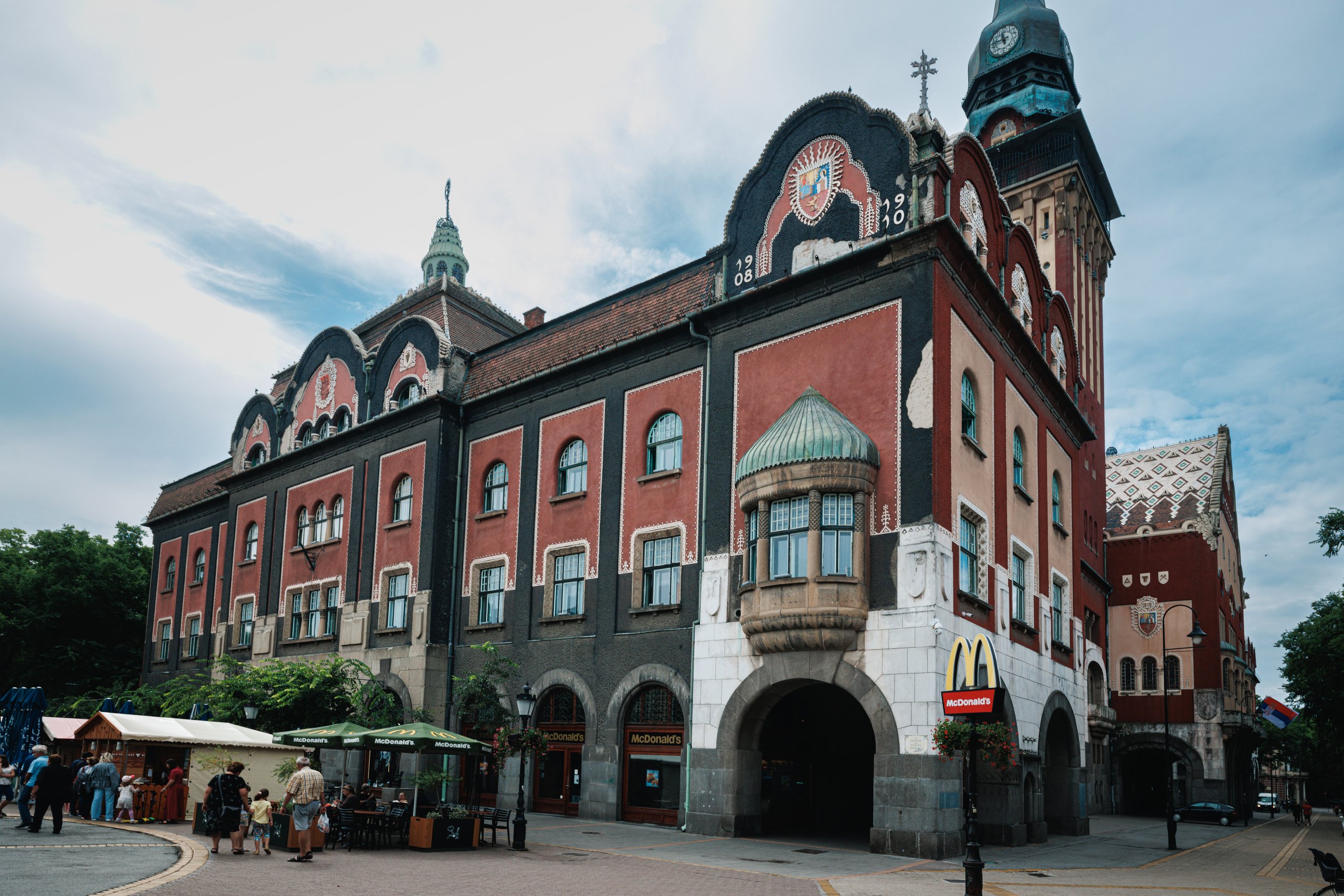 Subotica City Hall with red walls, patterned roofs and a small McDonald’s sign at street level.