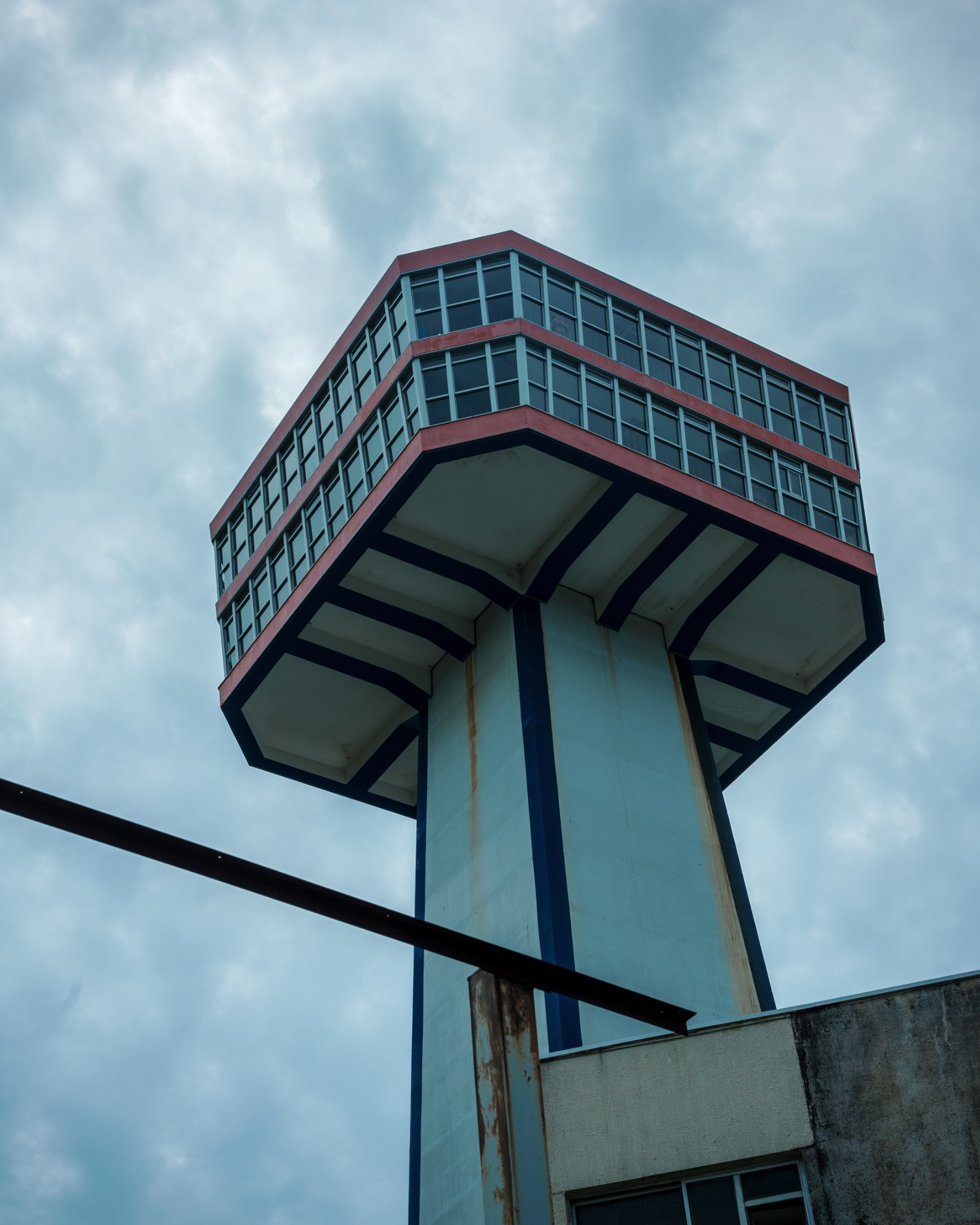 Low-angle view of Tojinbo Tower beneath a cloudy sky, showing the red-trimmed observation deck and weathered support column.