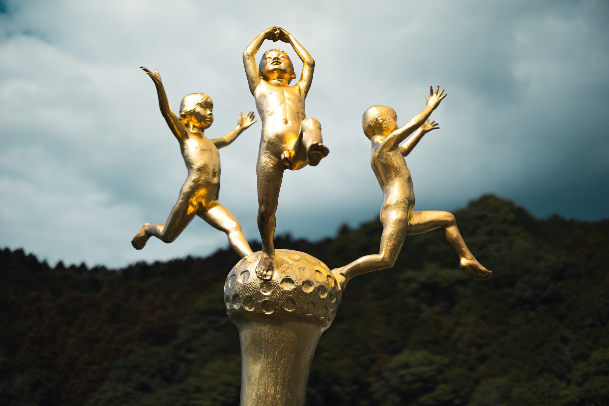 Close view of three golden child figures of Kazenko with outstretched arms and bent knees against the sky in Tsunagi, Kumamoto.