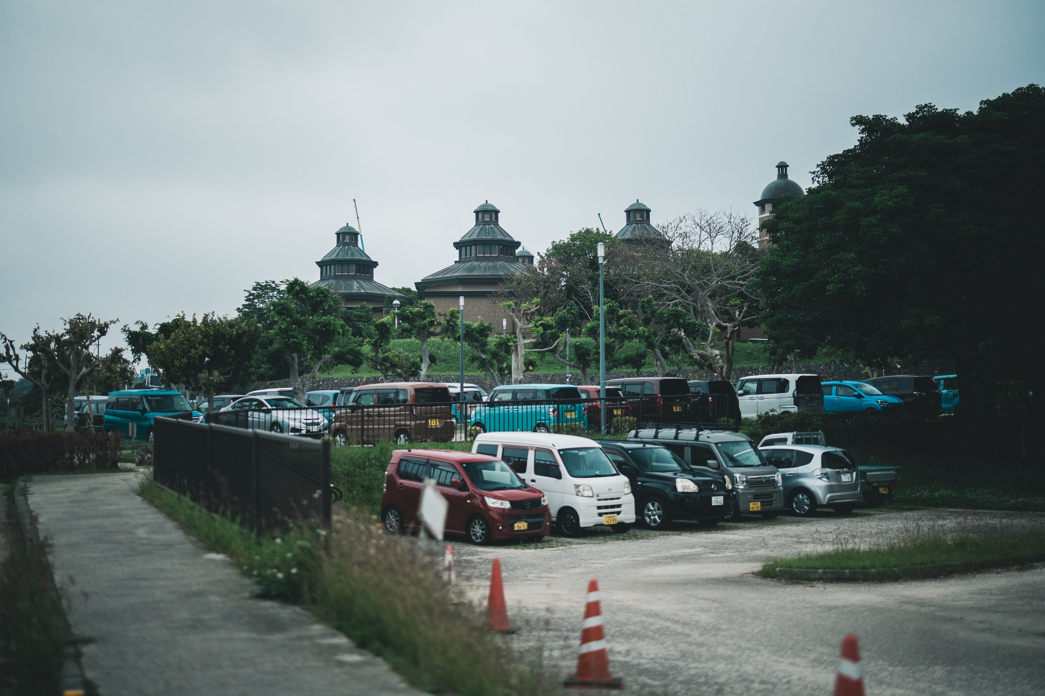 Tiered octagonal roofs of the Urasoe Art Museum rising behind rows of parked cars and traffic cones