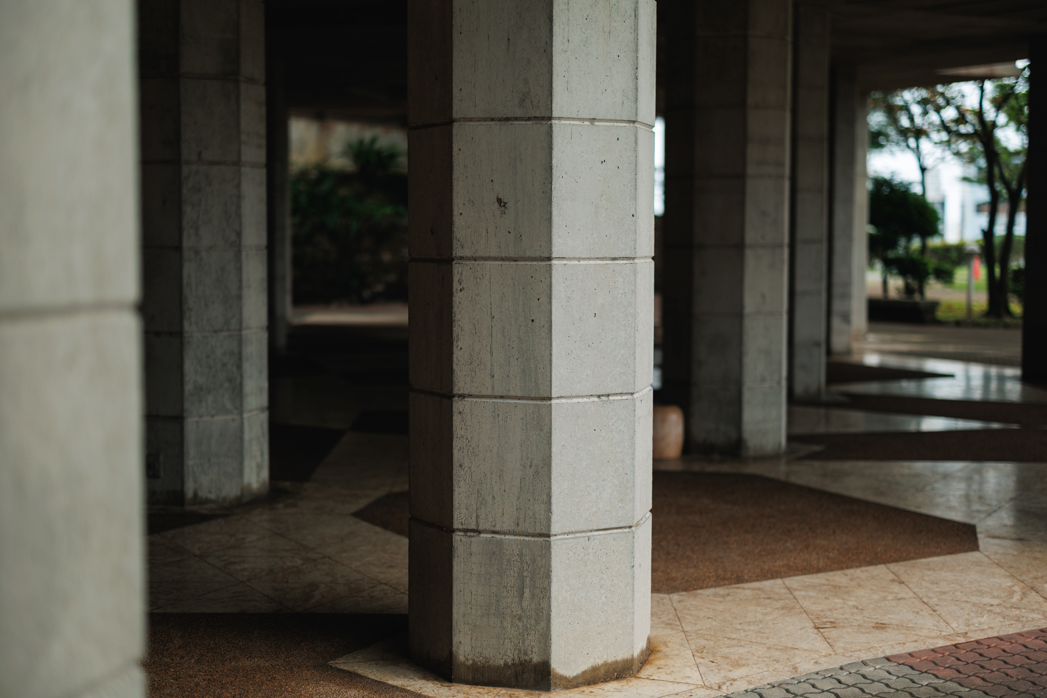 Octagonal concrete columns standing on a patterned stone floor beneath the museum, with trees beyond