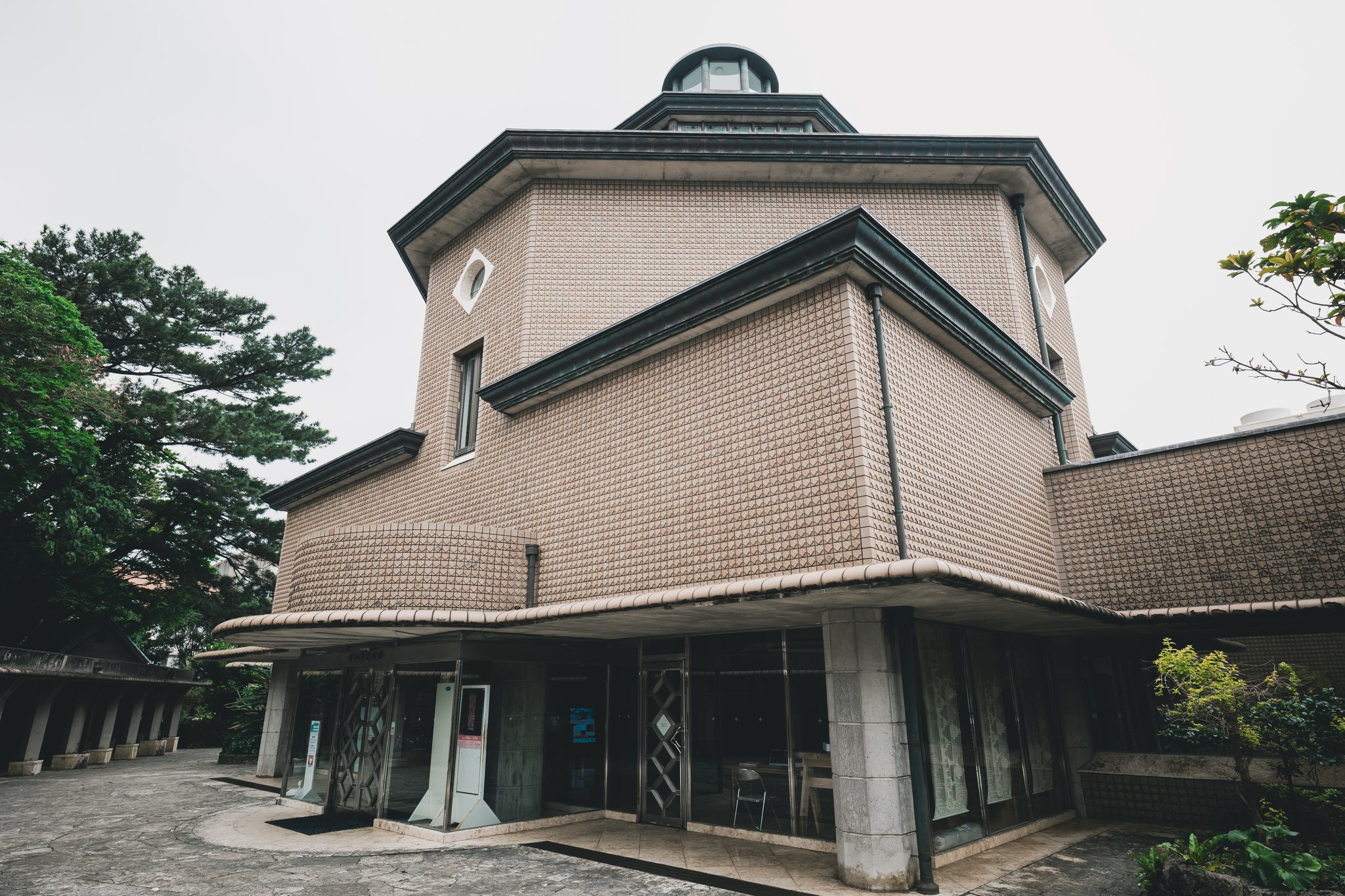 The entrance of the Urasoe Art Museum under a curved canopy, with textured brown tiles on the walls above and a small dome on top