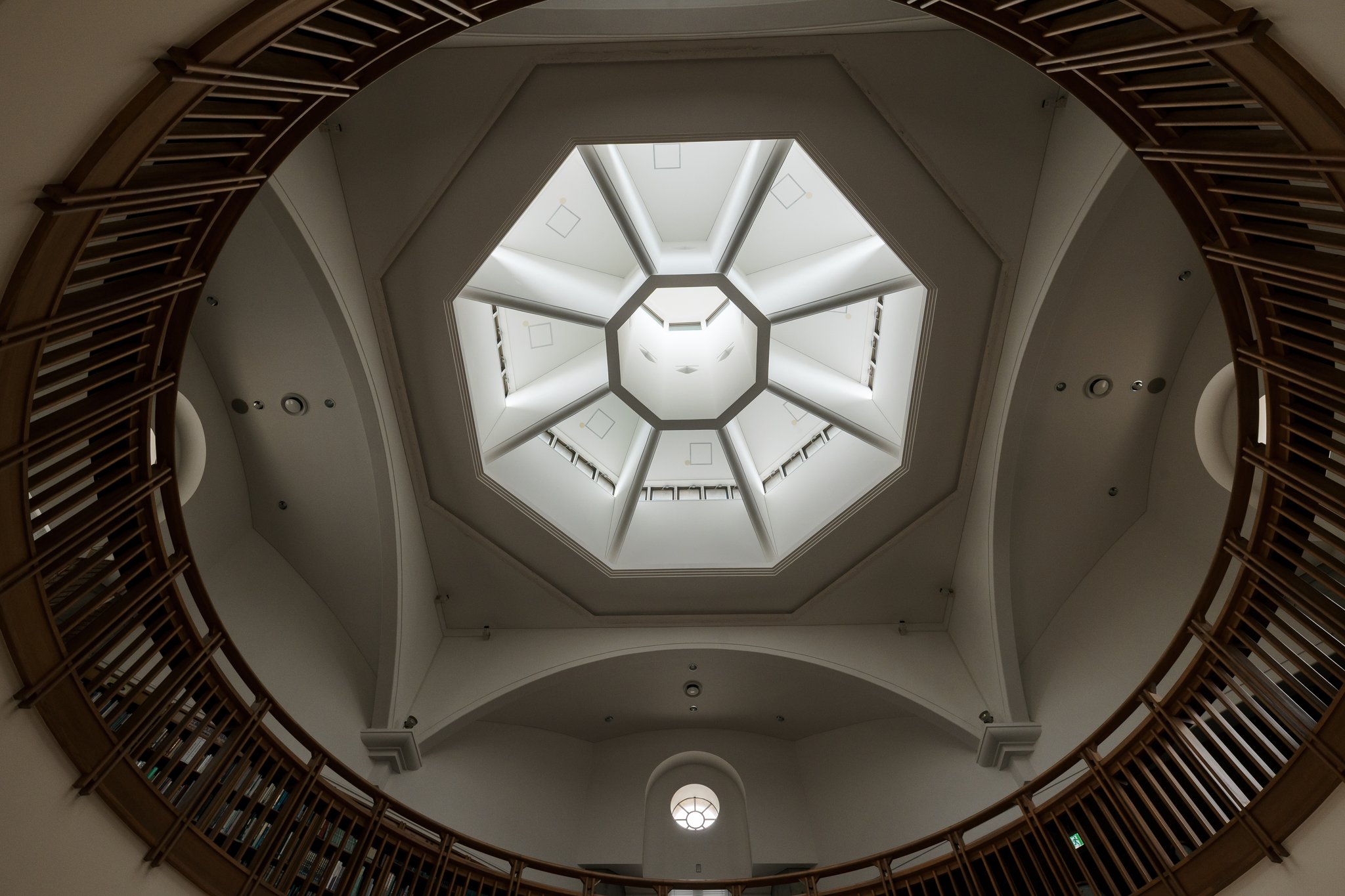 Looking up from the entrance hall at an octagonal skylight in a white dome, framed by a circular wooden railing with bookshelves