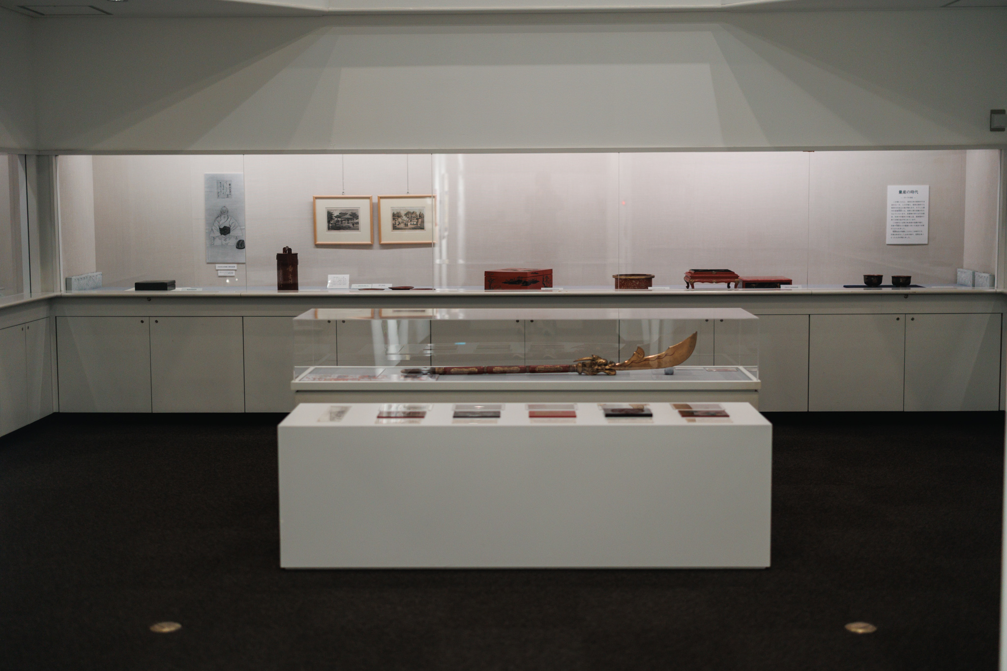 A gallery of the permanent collection, with red and black lacquerware in a long wall case and a dragon-headed piece in a central glass case