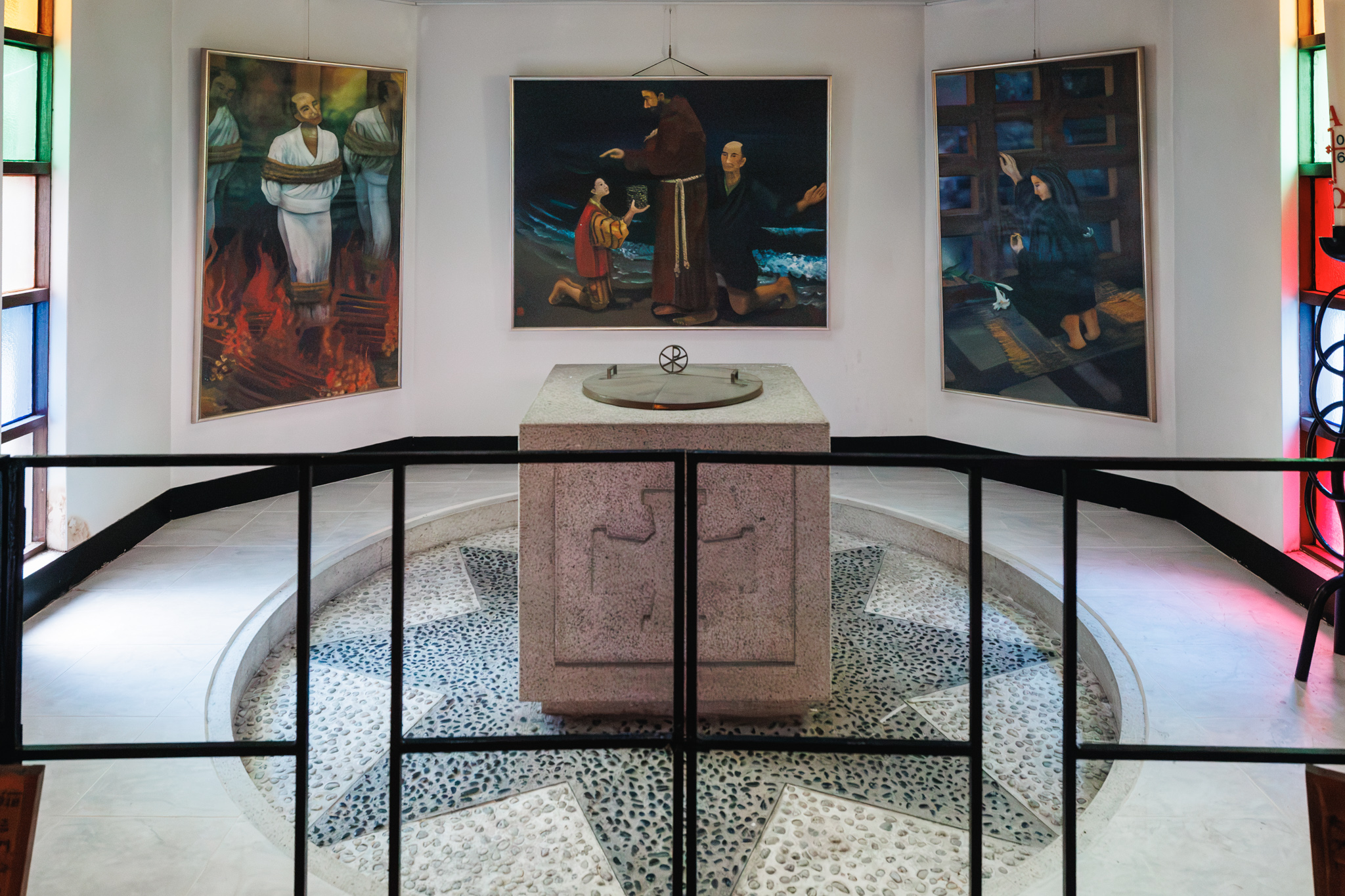 Three paintings by Kayoko Murata depicting Kamakura’s Christian history behind a stone baptismal font.